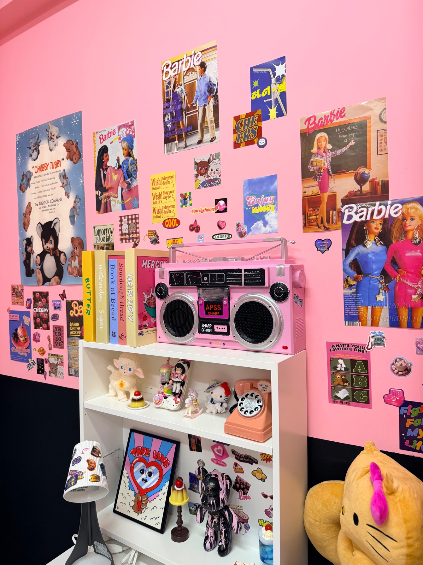 A pink wall of posters, a pink boombox and toys on a white shelf